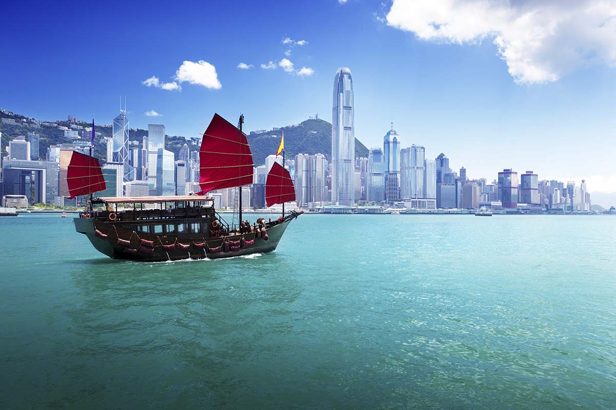 A boat with red sails in the water with Victoria Harbour in the background