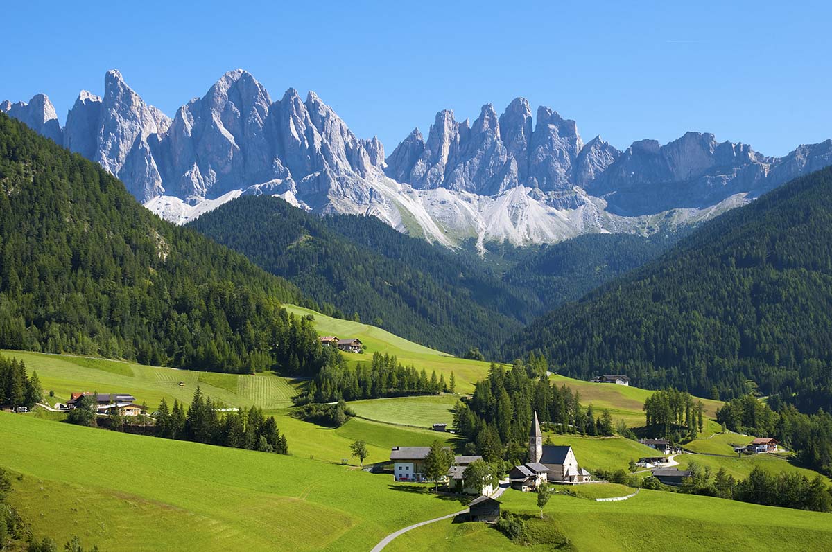 A green hills with trees and buildings in the background with Dolomites in the background