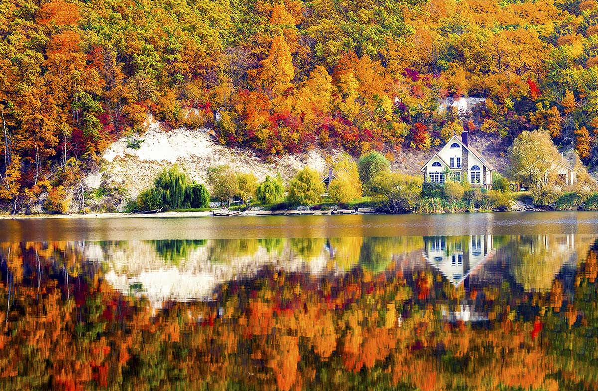 A house on the shore of a lake with trees and a hill