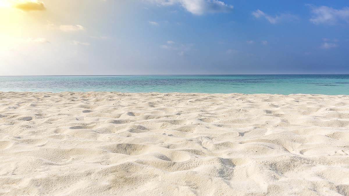 A sandy beach with blue water and blue sky