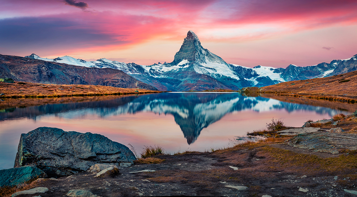 A mountain with a lake and a pink sky